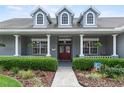 Inviting front porch with sturdy columns, a red front door, and lush landscaping along the walkway at 19624 Spring Oak Dr, Eustis, FL 32736