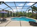 A relaxing screened-in pool area with a waterfall feature, lounge chairs, and lush tropical landscaping at 1053 Alcove Loop, The Villages, FL 32162