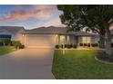 Charming single-story home with a well-maintained lawn and a two-car garage at sunset at 1813 Caryle Ln, The Villages, FL 32162