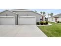 A modern one-story home with a gray exterior, two-car garage, and manicured lawn with bushes along the driveway at 27215 White Plains Way, Leesburg, FL 34748