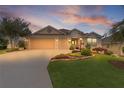Charming home with manicured front lawn, mature trees, and a two-car garage at dusk with a colorful sky at 627 Leeds Pl, The Villages, FL 32162