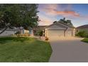 Charming single-story home with a well-manicured lawn, mature tree, and two-car garage at sunset at 898 Abaco Path, The Villages, FL 32163