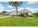 Beautifully landscaped yard with green lawn, palm tree, and flowering shrubs surround this bright single-story house at 1521 Southport St, The Villages, FL 32162