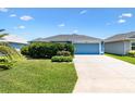 Charming single-story home featuring a well-manicured lawn, vibrant shrubs, and a two-car garage with a blue door at 2160 Biller Cir, The Villages, FL 32163