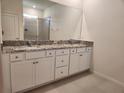 Bathroom features a dual sink vanity with granite countertop, a large mirror, and a walk-in shower at 6203 Sw 93Rd Loop, Ocala, FL 34476