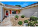 Inviting front porch with decorative gravel, potted plants, and red door with glass at 1206 Thompson Ave, The Villages, FL 32162