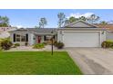 Inviting single-story home with a well-maintained lawn, a two-car garage, and colorful plants at 2712 Plainridge Loop, The Villages, FL 32162