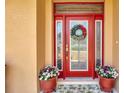 An inviting red front door is flanked by flower-filled pots and a glass-paneled sidelight at 4716 Heritage Trl, Leesburg, FL 34748