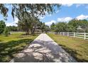 Long driveway lined with white fencing leads to the stunning home surrounded by lush greenery on a sunny day at 21206 Canoe Pass St, Clermont, FL 34715