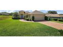 Well-manicured lawn and shrubbery surround a charming one-story home with a brick driveway and two-car garage at 39504 Hillrise Ln, Lady Lake, FL 32159