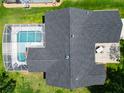 Aerial view of a home with a screened-in pool, patio area, and dark shingled roof surrounded by lush landscaping at 750 Eden Pl, The Villages, FL 32162