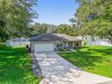 Well-manicured lawn leading to a charming home, surrounded by mature trees and featuring a spacious driveway and two-car garage at 9364 Se 164Th Pl, Summerfield, FL 34491