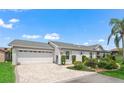 Charming home features a two-car garage, brick driveway and walkway, trimmed bushes, and landscaped flower beds at 17380 Se 111Th Ct, Summerfield, FL 34491