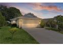 A home exterior is seen at dusk with a paved driveway leading to the garage, surrounded by mature landscaping at 2821 Mediterranean Loop, Tavares, FL 32778