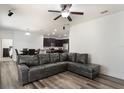 Open living space with wood floors, a large sectional couch, ceiling fan and an open view into the kitchen at 686 Black Eagle Dr, Groveland, FL 34736