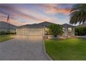 Charming home featuring a three car garage, well maintained lawn, and tropical landscaping at sunset at 2082 Vision Ct, The Villages, FL 32163