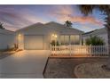 The home's exterior is beautifully illuminated at twilight, highlighting the white picket fence at 9321 Se 172Nd Augusta Ln, The Villages, FL 32162