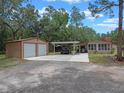 Property featuring a two-car garage, a carport, and a home with a red roof, surrounded by lush greenery at 12288 Sw 35Th Dr, Webster, FL 33597