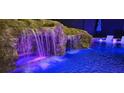 A stunning pool featuring a rock waterfall and slide, illuminated with colorful lighting for nighttime enjoyment at 14501 Wabasso Loop, Winter Garden, FL 34787