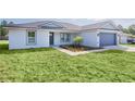 Charming single-story home featuring a blue garage door, grey roof, and nicely landscaped front yard at 472 Malauka Radl, Ocklawaha, FL 32179