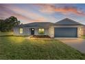 Charming single-story home with a blue garage door, grey roof, and nicely landscaped front yard at dusk at 472 Malauka Radl, Ocklawaha, FL 32179