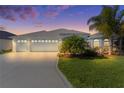 Beautiful home featuring a three-car garage, light-blue exterior, well-manicured lawn, and decorative driveway at dusk at 4878 Chitty Chatty Run, The Villages, FL 32163