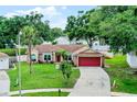 Inviting single-Gathering home with mature trees, well-maintained lawn, and a red garage door at 15916 Indian Wells Ct, Clermont, FL 34711