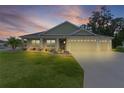 Beautiful single-story home featuring a three-car garage and a well-manicured lawn at twilight at 6991 Sugar Creek Path, The Villages, FL 34762