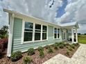 Side view of a light green house with large windows, white trim, and manicured landscaping at 12110 Grand Oak Ln, Oxford, FL 34484