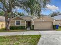 Inviting single-story home with a tan exterior, two-car garage, and manicured front yard, perfect for a Gathering at 2019 Newtown Rd, Groveland, FL 34736