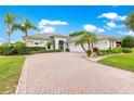 Inviting white facade with well-kept shrubs and palm trees, leading to a brick paved drive and a multi-car garage at 39145 Treeline Dr, Lady Lake, FL 32159