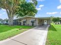 Single-story home with a long driveway, covered carport, and neatly maintained lawn, showcasing curb appeal at 1005 Richard Dr, The Villages, FL 32159