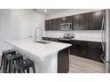 Open kitchen with counter seating, featuring stainless steel appliances, dark cabinetry, and quartz countertops with wood floors at 1696 Wilson Prairie Cir, Groveland, FL 34736