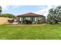 Wide backyard showcasing a well-maintained lawn, palm trees, a patio with outdoor furniture, and the exterior of the home at 2585 Constance Ct, The Villages, FL 32163