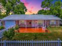 Charming brick home with a vibrant orange porch and a white picket fence under a colorful sunset sky at 564 Lancaster Ave, Orange City, FL 32763