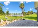 Beautiful backyard with a brick patio, mature palm trees, and stunning lake views beyond the green lawn at 5746 Botner Dr, The Villages, FL 32163