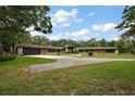 Expansive exterior with mature trees, long driveway, wooden home with stone accents, and a side-entry two-car garage at 672 E Belt Ave, Bushnell, FL 33513