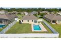 Aerial shot of the backyard featuring a clean in-ground pool surrounded by green lawn and a white fence at 9785 Pepper Tree Trl, Wildwood, FL 34785