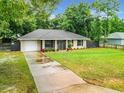 Exterior view featuring a well-manicured lawn, driveway, and partial fence surrounding the charming single story home and attached garage at 12181 Se 87Th Ct, Belleview, FL 34420