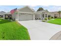 View of the home's gray concrete driveway, attached two-car garage, tidy front yard, and an American flag at 3057 Saint Thomas Ln, The Villages, FL 32162
