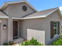 Exterior angle showing tan stucco and a dark front door, complete with a circle vent and window with shutters at 6946 Perch Hammock Loop, Groveland, FL 34736