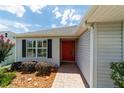 Close-up of home's entrance showcasing the red front door, black shutters, and brick paver walkway at 16730 Se 78Th Lillywood Ct, The Villages, FL 32162