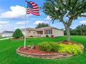 Lush front yard featuring mature tree, brick-lined garden, and American flag adds to the property's curb appeal at 1948 Harston Trl, The Villages, FL 32162