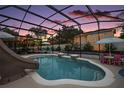 A beautiful screened pool with a slide and patio furniture sits in a private backyard under a twilight sky at 318 Stone Castle Loop, Lady Lake, FL 32159