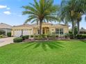 Inviting home featuring manicured landscaping with palm trees, flowerbeds, and a green lawn at 591 Allenwood Loop, The Villages, FL 32162