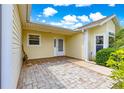 Covered back porch with brick flooring, features a white door and is surrounded by vibrant green foliage at 2450 Merida Cir, The Villages, FL 32162