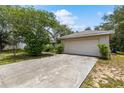 Two-car garage with a wide driveway, nestled in a grassy yard with mature trees and a clear blue sky at 9879 Sw 38Th Ave, Ocala, FL 34476