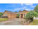 Tan house with a two-car garage, lush landscaping, and a brick paver driveway at 178 Magneta Loop, Auburndale, FL 33823