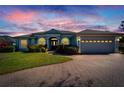 Gray house with a three-car garage, and a brick driveway under a sunset sky at 7068 Island Lake Ln, Lakeland, FL 33813