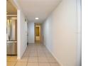 Hallway with neutral tile flooring leads to the kitchen with stainless steel fridge and bathroom at the end at 474 Cameo Dr, Lakeland, FL 33803